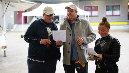 Drei Mitarbeitende blicken stehen im Festzelt und schauen auf Blätter mit einem Liedtext bei der Jubiläumsfeier 20 Jahre Albertinen Services Hamburg ASH in Rellingen.