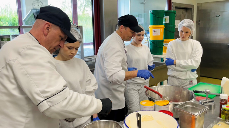 Mitarbeiter der Zentralküche zeigen Schülerinnen beim Girls’ Day praktische Arbeitsschritte bei der Zubereitung von Speisen.
